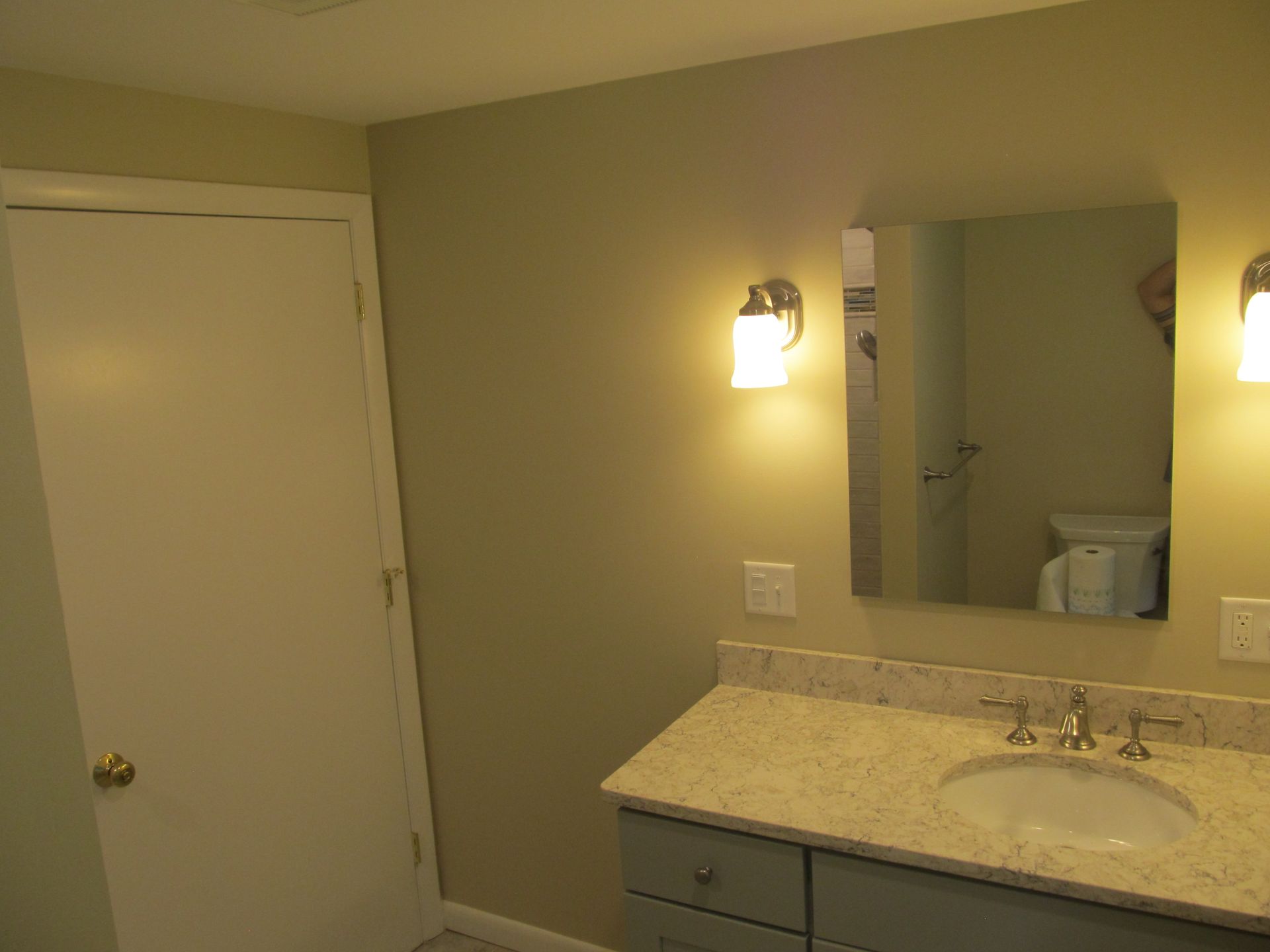 Bathroom vanity with mirror, light fixture, and beige walls beside a white door.