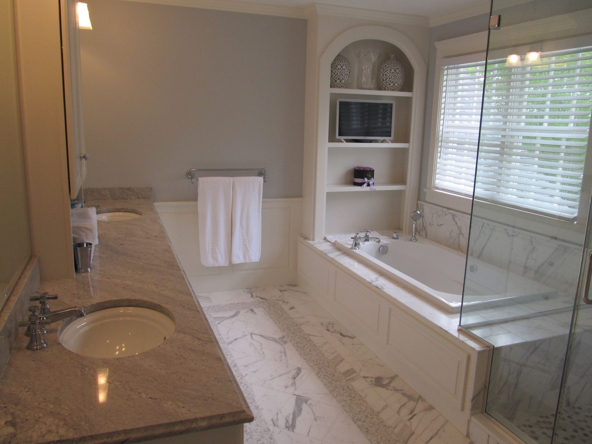 Bright bathroom with double sinks, large bathtub, and window blinds, finished in beige and white.