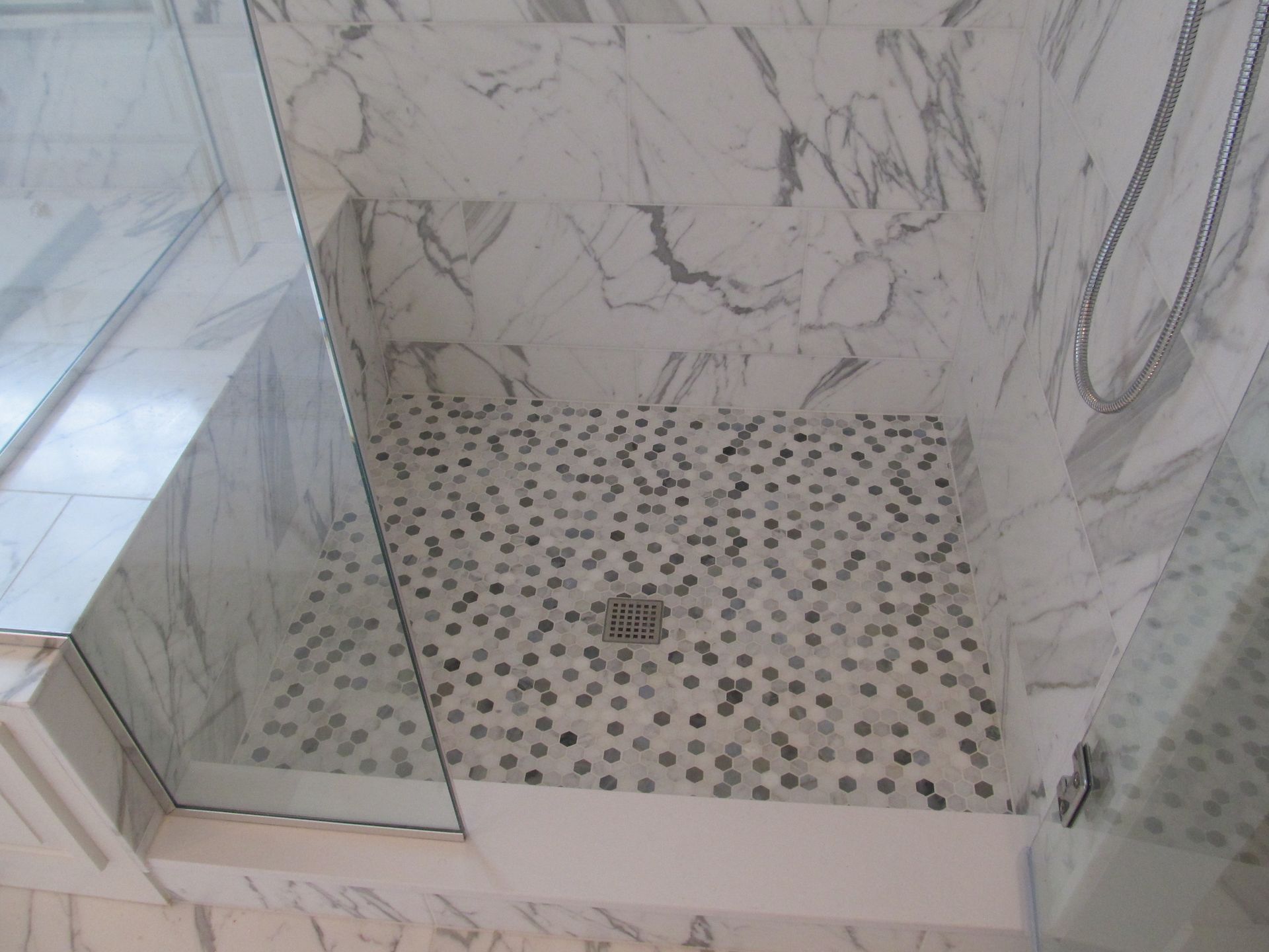 Marble-tiled walk-in shower with glass door and pebble mosaic floor