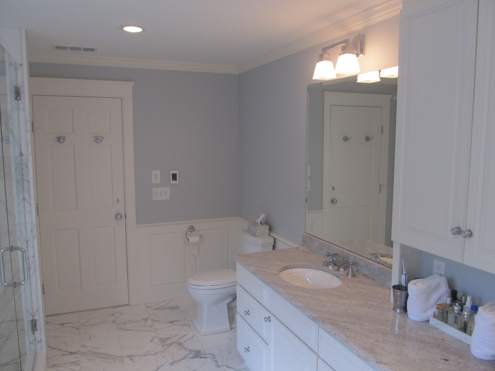 Bathroom with white cabinets, marble vanity, toilet, and tub under soft overhead lighting