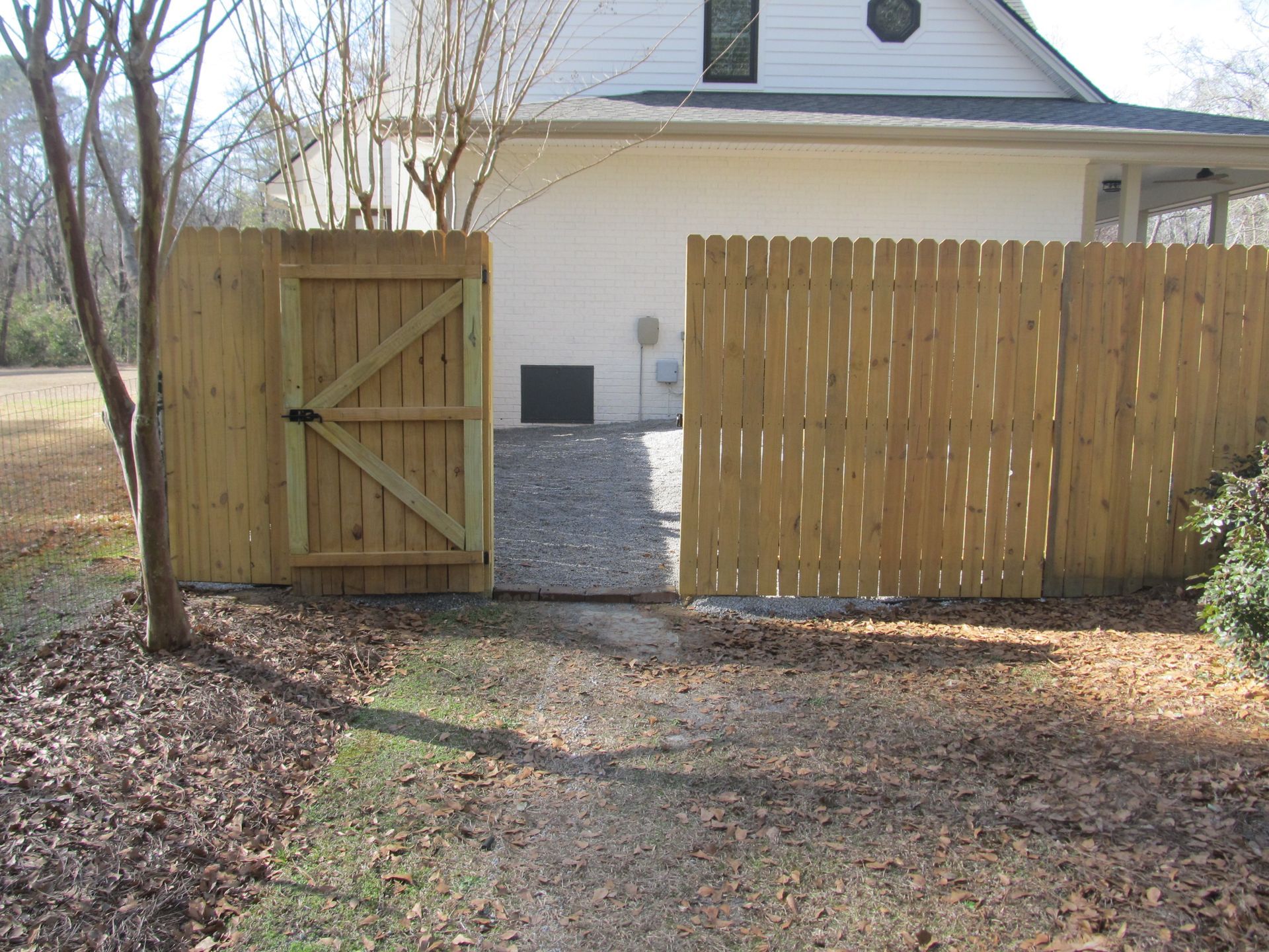 Wooden gate and fence opening to a gravel driveway beside a white house