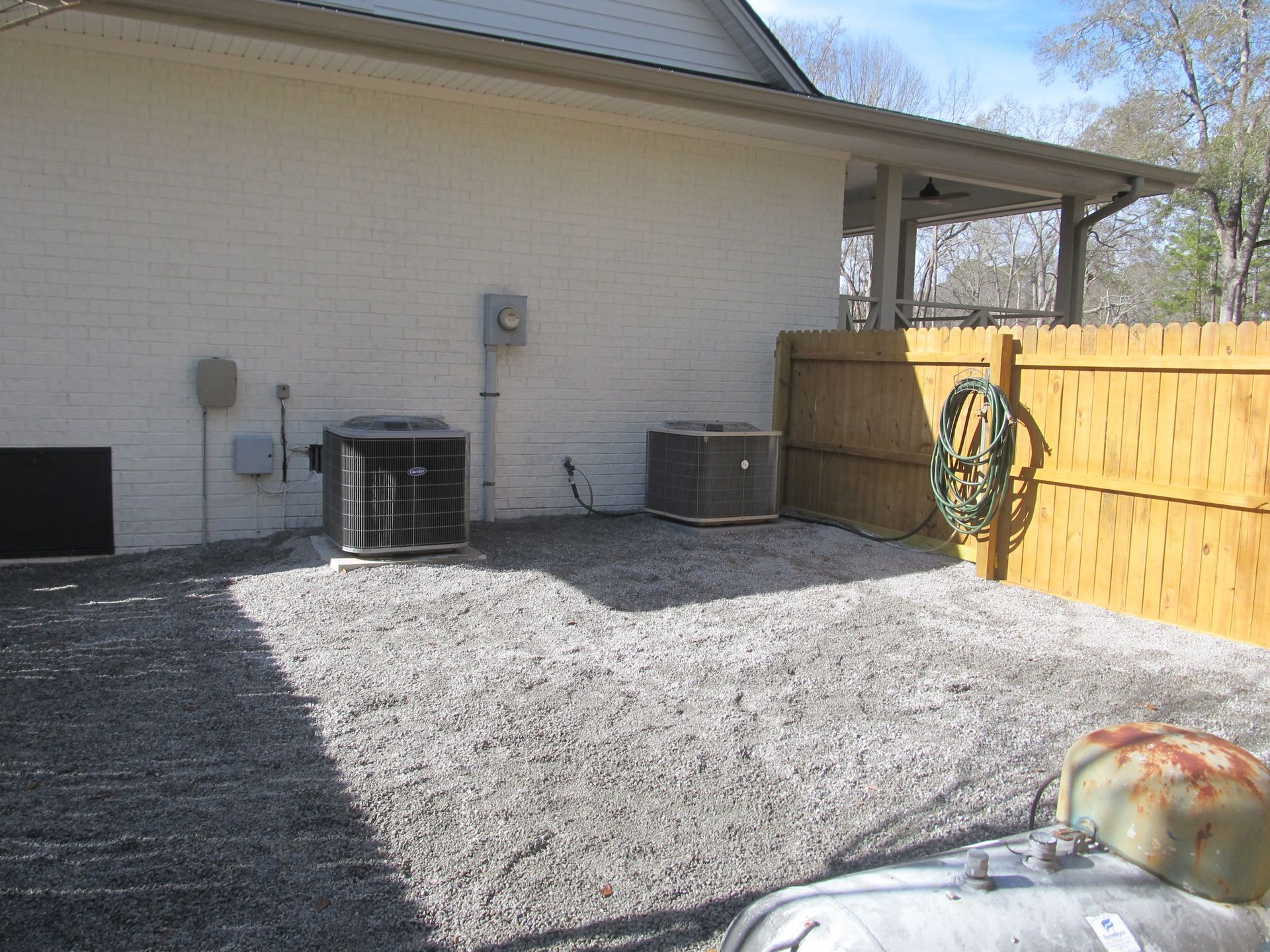 Backyard with gravel patio, two HVAC units, and a wooden fence with a hose reel.