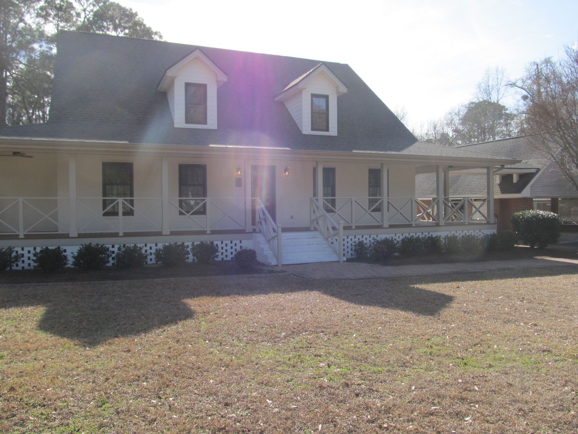 White house with porch and dormer windows, front yard, bright sunlight and lens flare