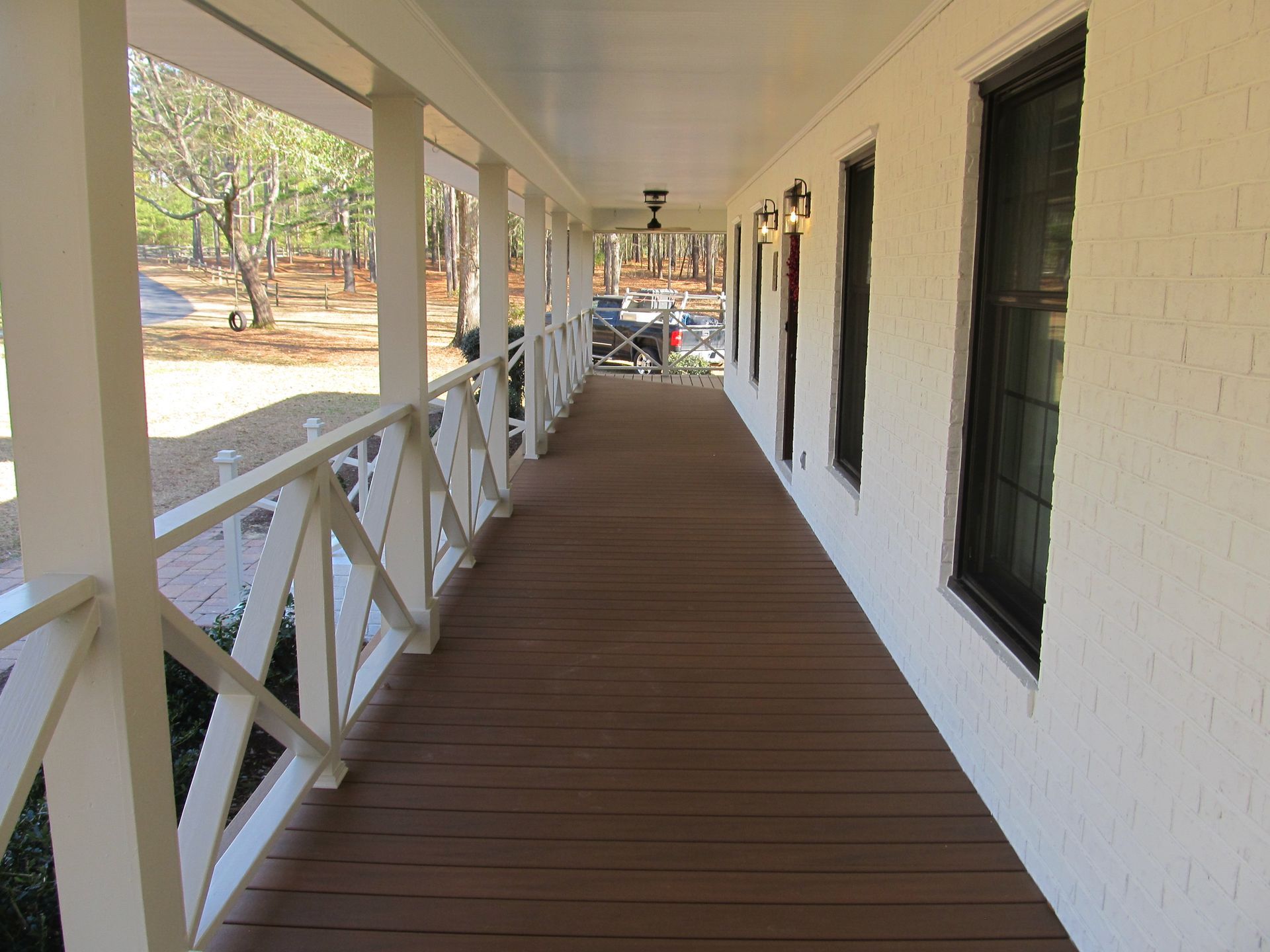 Long wooden porch walkway with white railings beside a beige house in daylight