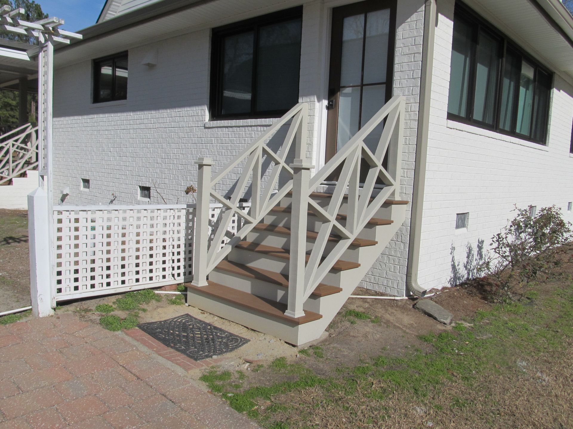 White house exterior with front steps, railing, and a small lattice gate beside a walkway