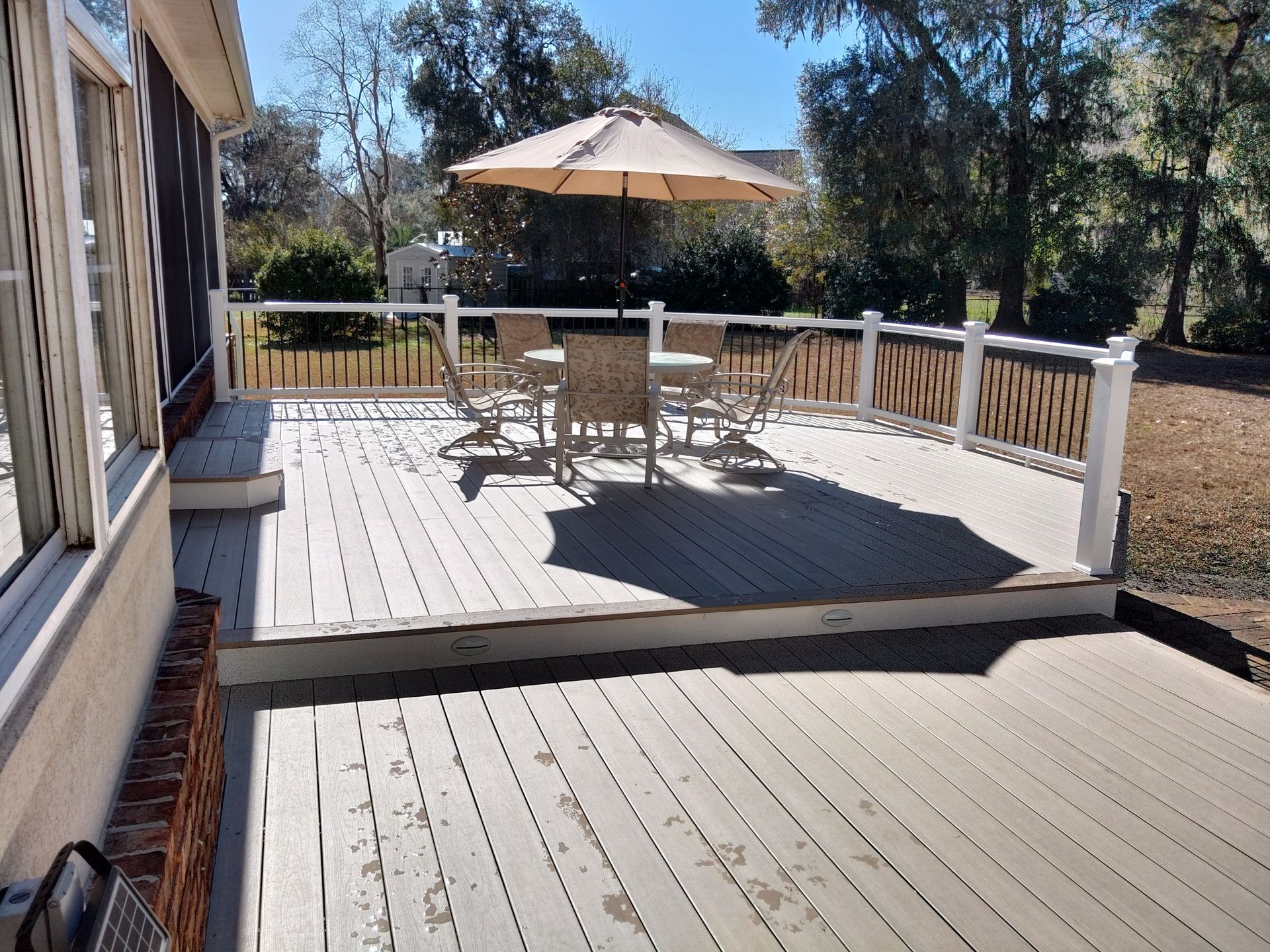 Wooden deck with outdoor table, chairs, and beige umbrella in a sunny backyard