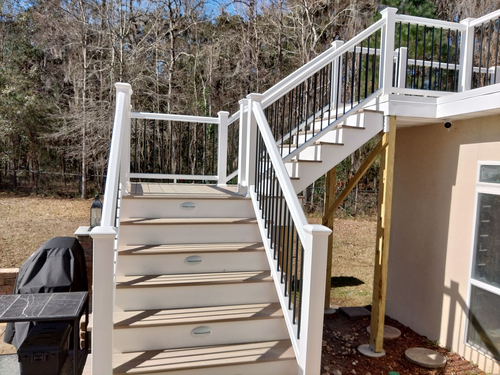 Outdoor beige stairs with white railings leading up to a deck beside a house