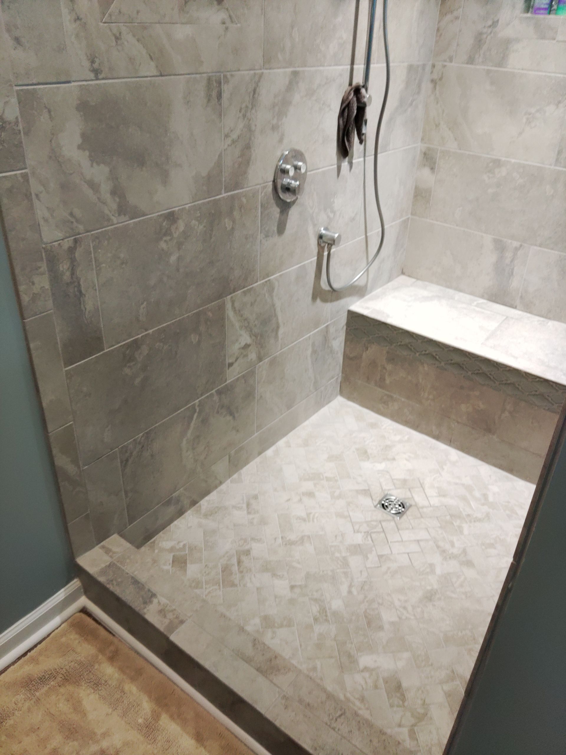 Tiled walk-in shower with built-in bench, chrome fixtures, and a recessed shower floor