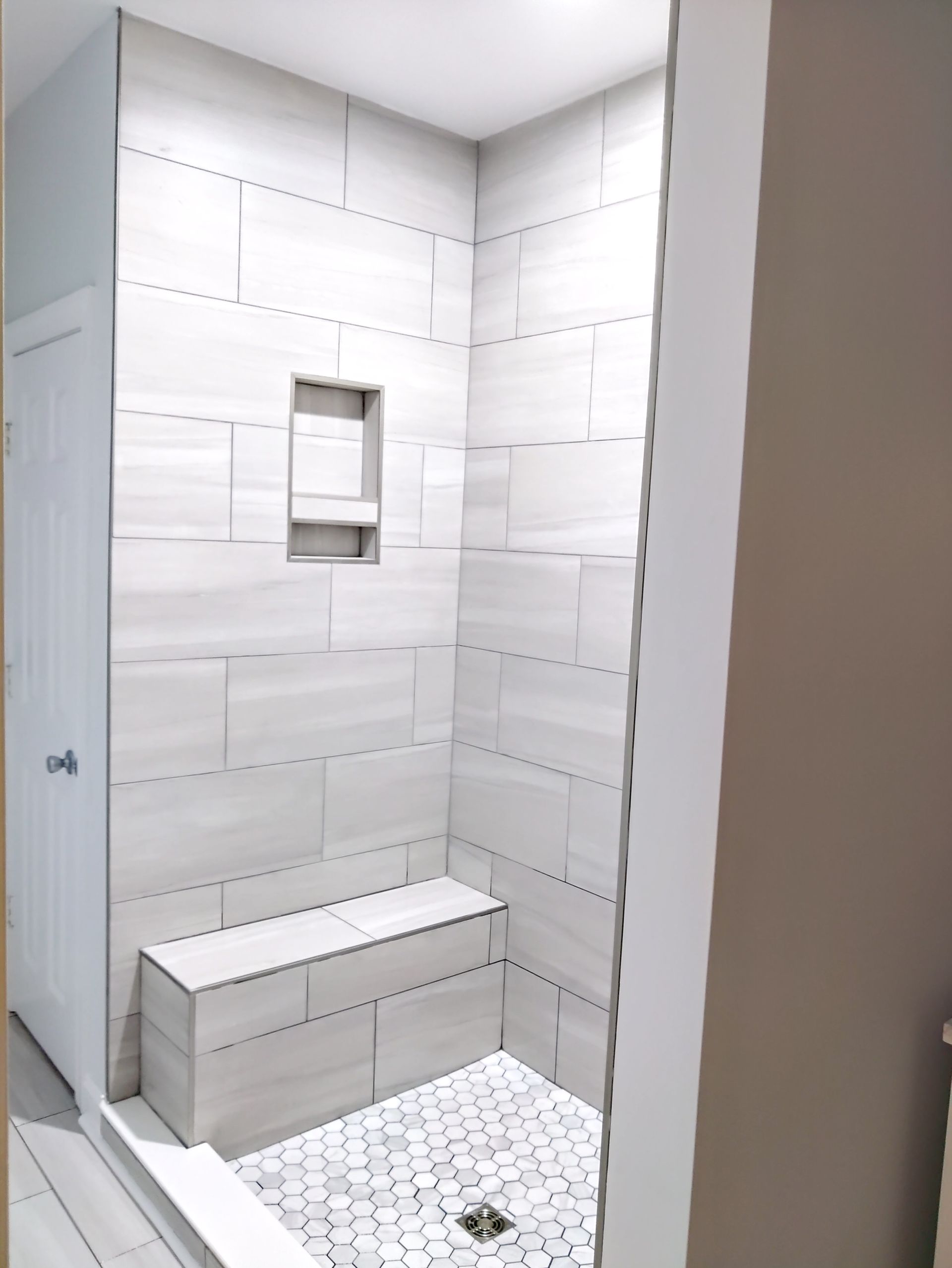 Small tiled shower with a built-in bench, window niche, and white hexagon floor tiles.