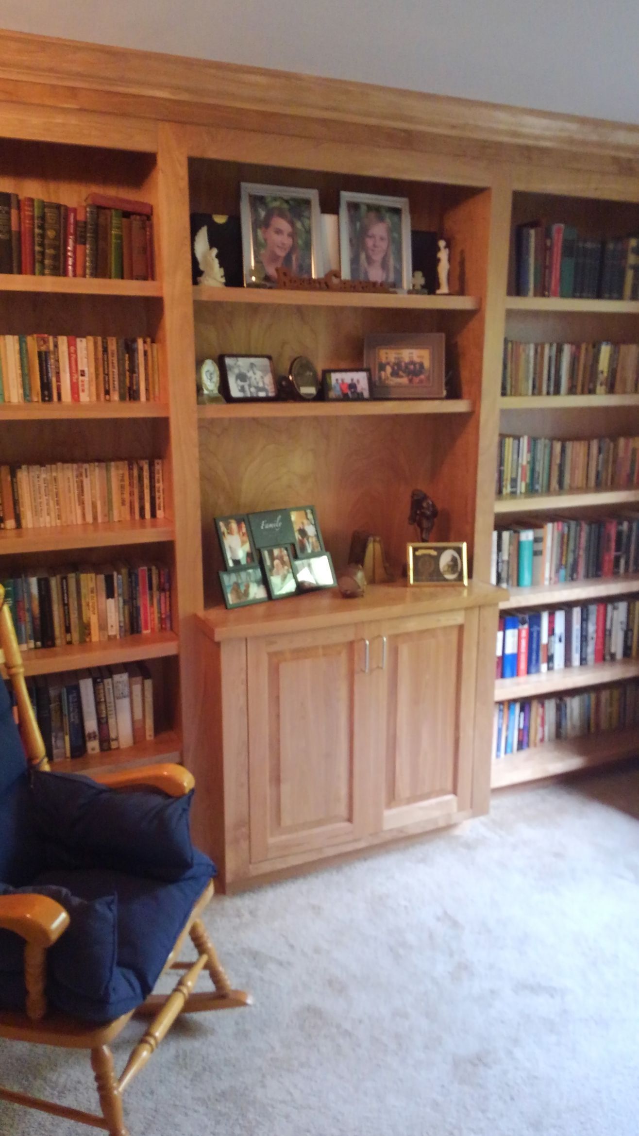 Wood-paneled bookshelf wall with books, framed photos, and a blue chair in a carpeted room