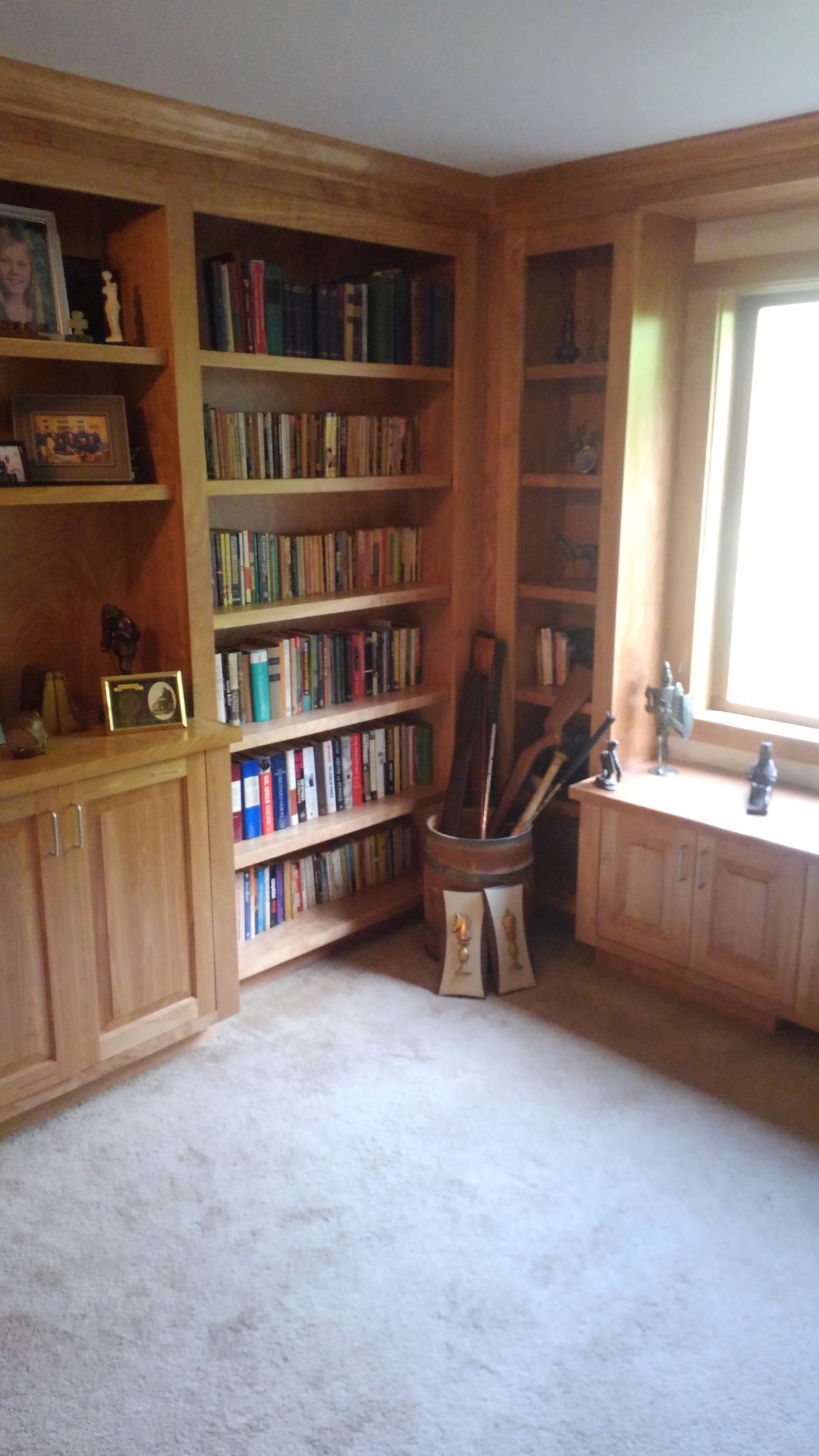 Cozy corner with built-in bookshelves, wooden cabinets, and a bright window seat in a carpeted room