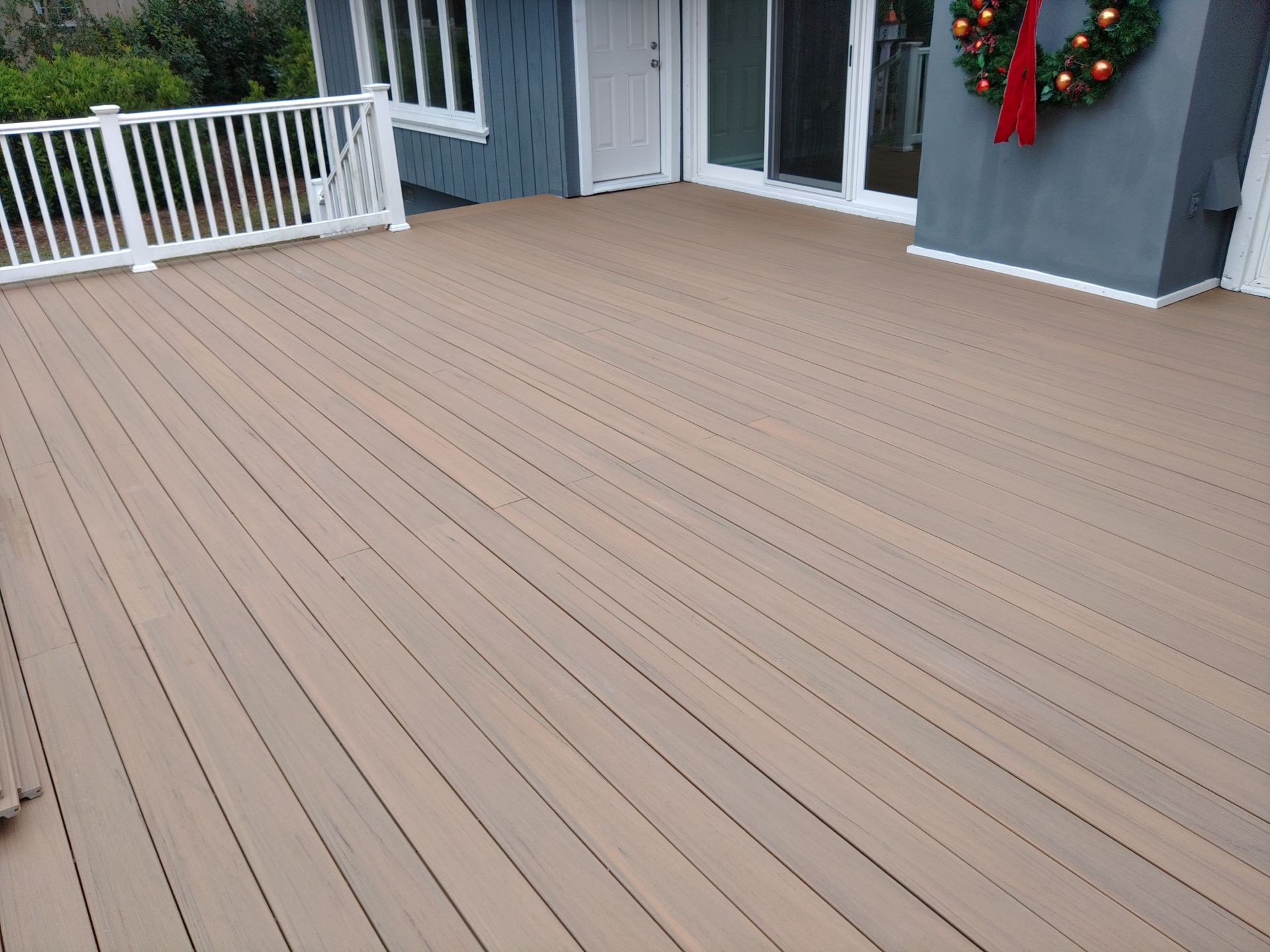 Empty wooden deck outside a gray house with white railing and holiday wreaths