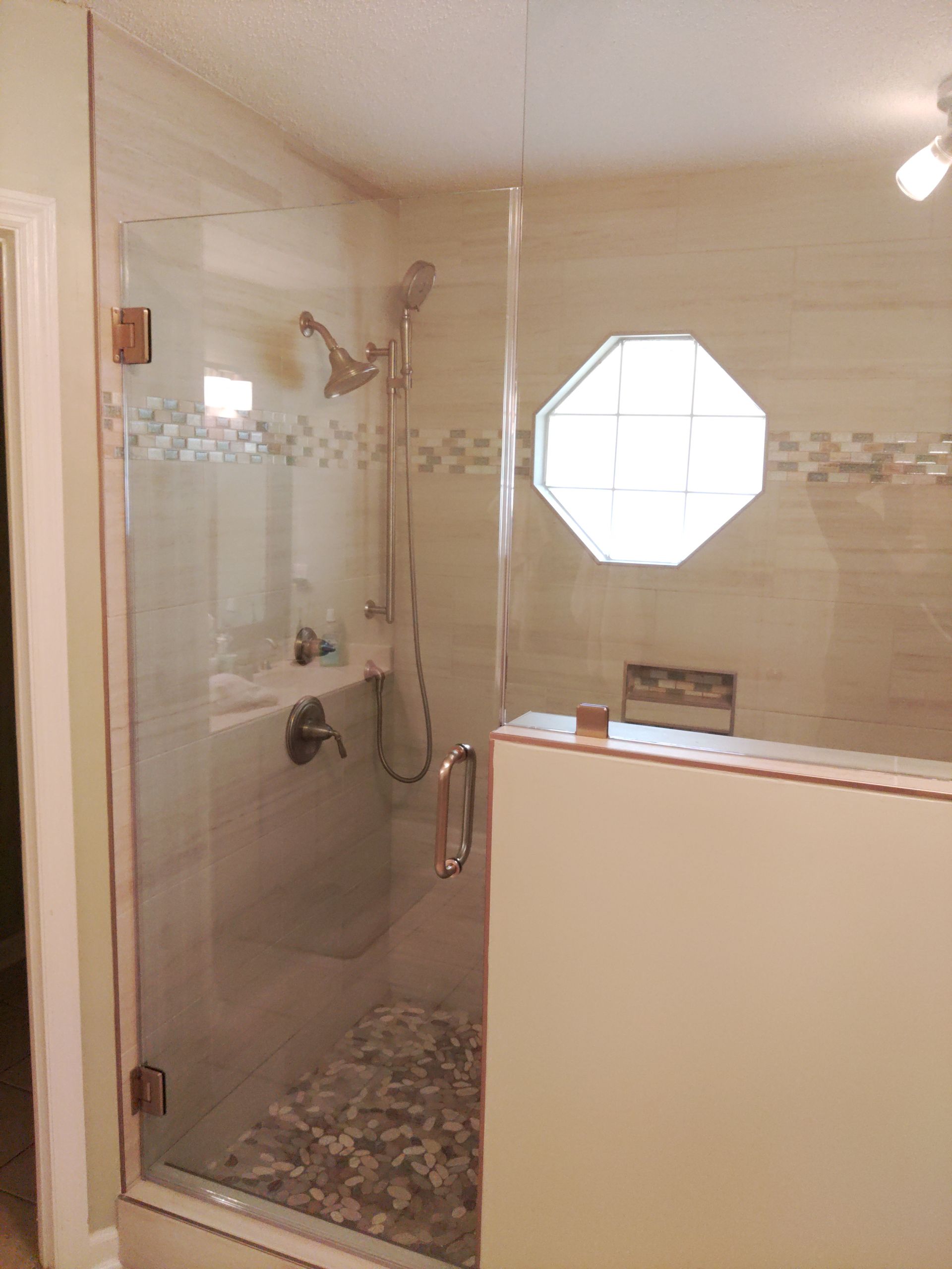 Bathroom with a glass-enclosed shower, tiled walls, and an octagonal window.