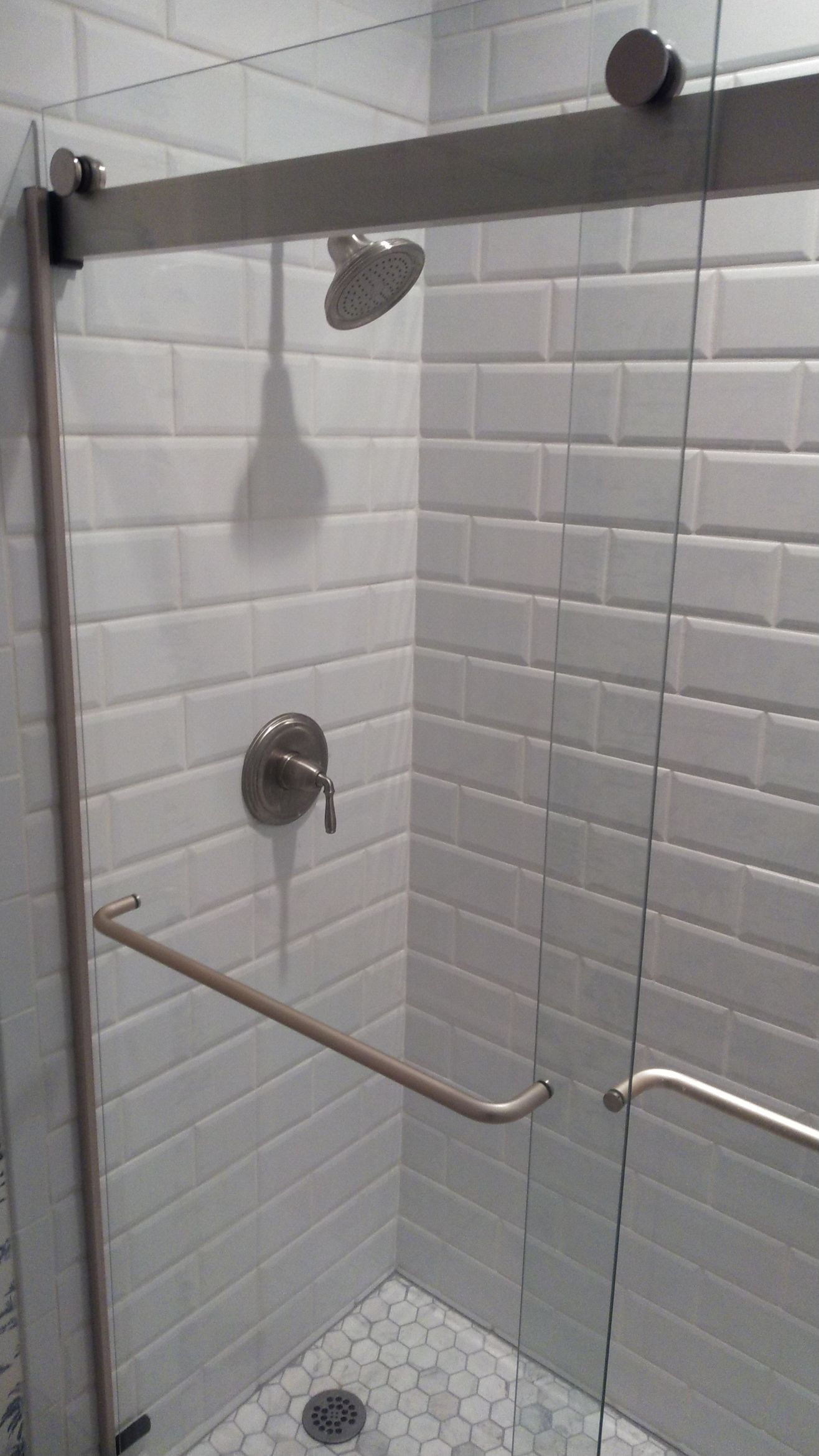 Accessible shower stall with white tile walls, grab bars, and a handheld showerhead