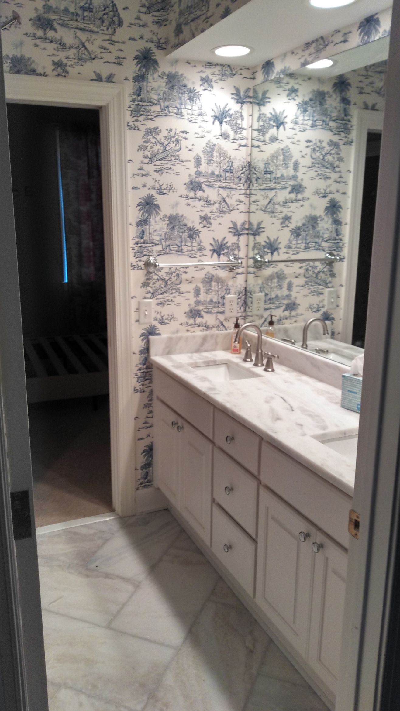 Bathroom with blue-and-white toile wallpaper, white vanity, sink, and mirror under bright lights
