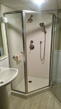 Small accessible shower stall with glass doors, wall-mounted showerhead, and handheld sprayer in a bathroom.