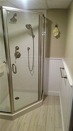 Corner shower with glass door in a small bathroom, beige tile walls and light wood floor.
