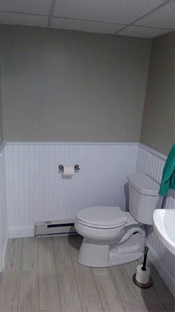 Small bathroom with a toilet, sink, white wainscoting, and a wall-mounted toilet paper holder.