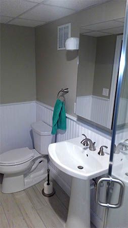 Bathroom with toilet, sink, mirror, and shower, featuring green towel and white tile walls