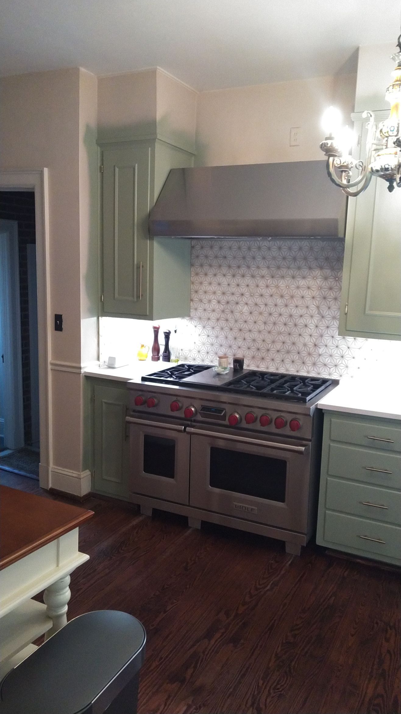 Modern kitchen with green cabinets, stainless stove, tiled backsplash, and dark wood floor.