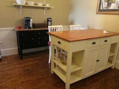 Kitchen with a wooden island, black side cabinet, and wall shelves in a bright room