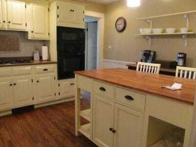 Small kitchen with cream cabinets, wood floor, island, and wall shelves by a doorway.