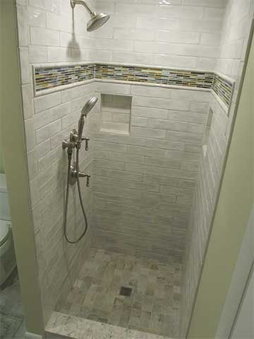 Small tiled shower stall with handheld showerhead and mosaic accent border.