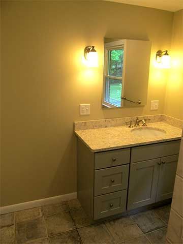 Small bathroom vanity with mirror, wall sconces, gray cabinets, and tiled floor.
