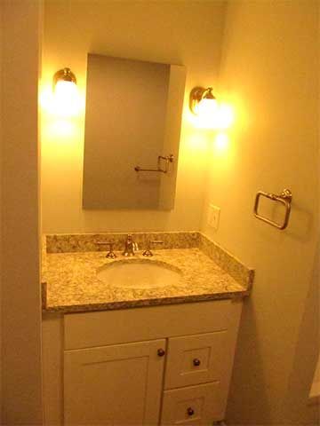 Small bathroom vanity with granite countertop, mirror, wall sconces, and towel ring in warm yellow light