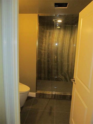Narrow bathroom with a toilet, dark tiled floor, and shower stall with glass door.