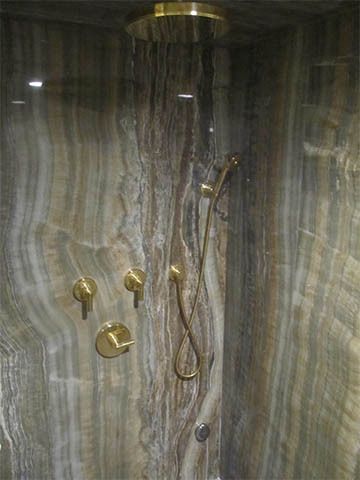Marble shower stall with gold fixtures, handheld shower, and a glass door partially open