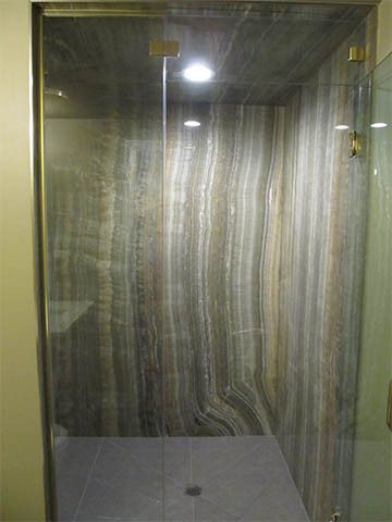 Empty marble-tiled shower stall with glass door and drain.