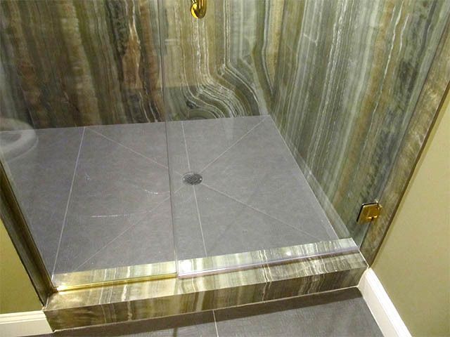 Glass shower enclosure with gray tiled floor and brass trim