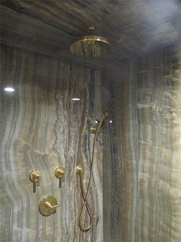 Marble-tiled shower with gold fixtures and a handheld showerhead.