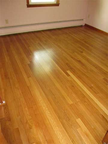 Empty room with glossy hardwood floor and white walls, lit by a window.
