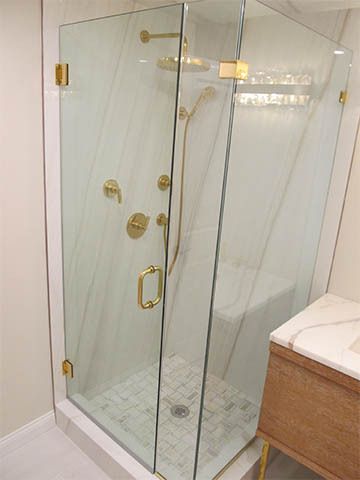 Glass corner shower with brass fixtures and marble tile floor in a bathroom