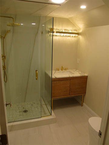 Modern bathroom with glass shower, wooden vanity, and recessed ceiling lights.
