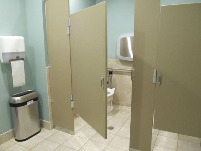 Public restroom with beige stall doors, a sink, trash can, and a hand dryer visible.