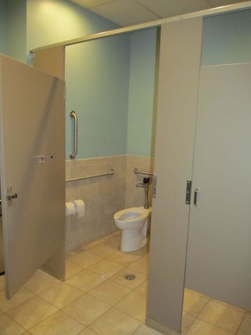 Accessible restroom stall with open doors, toilet, grab bars, and beige tiles