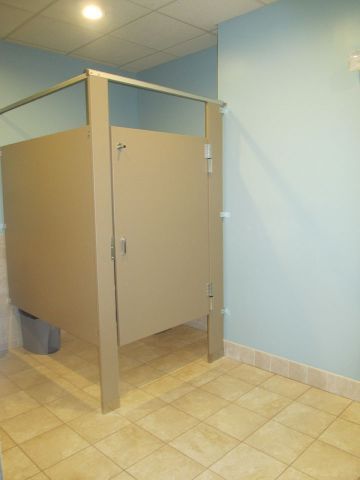 Public restroom stall with beige doors and partitions on a tiled floor