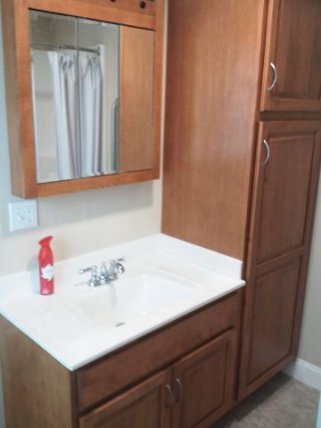 Bathroom vanity with wood cabinets, white sink, mirror, and red soap dispenser