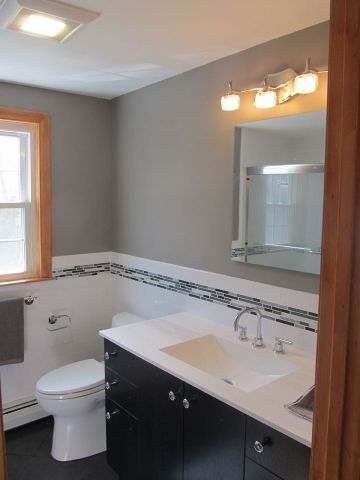 Bathroom with toilet, vanity sink, mirror, and window, accented by gray walls and white tile trim