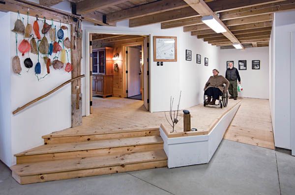 Indoor museum gallery with wooden steps, wall art, and two people seated on benches