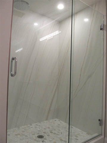 Glass shower stall with white marble tile walls and a tiled floor.