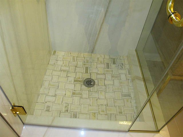 Glass shower stall with beige tiled floor and center drain