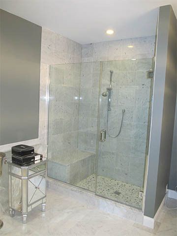 Modern bathroom with a glass walk-in shower and a chrome side table with folded towels