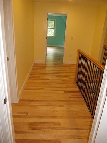 Empty yellow hallway with hardwood floor and black railing, leading to a green room.