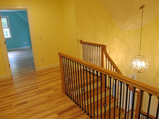 Staircase with wooden railing in a yellow hallway, lit pendant lamp, and blue room visible in the background