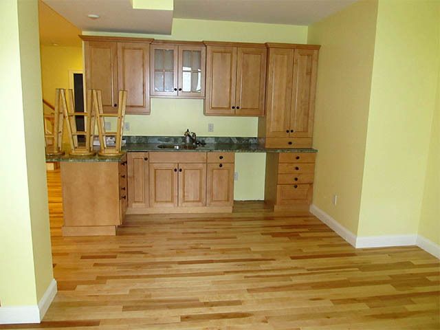 Empty kitchen with wooden cabinets, light wood floor, and yellow walls in a small room.