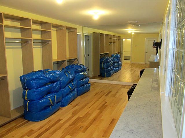 Room with wooden floors and built-in shelves, cluttered with stacked blue bags and moving supplies.